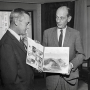 Melvin J. Roberts, right, president of the Denver Clearing House Assn., holds up a copy of the Denver Olympic Committee's presentation book, used to win the United States competition. Roberts was presented with [the] book by Thomas Hildt, Jr., vice-president of finance for the Denver Olympic Committee, after receiving a check for $10,000 as This year's contribution from the assn. The money will be used in the DOC's 1968 budget for promotional expenses to win international designation for 1976 Winter games.