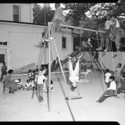 Children of all ages play on a swingset and slide on the George Washington Carver Day Nursery playground at 2357 Clarkson. Several students listen to a teacher telling a story