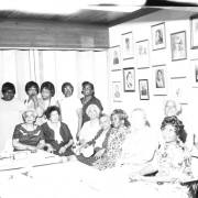 A group of thirteen women, possibly some of the school's original founders, sit in a meeting room in the George Washington Carver Day Nursery building at 2270 Humboldt Street. There are portraits of the school founders on the wall behind them.
