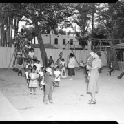 Young children of a variety of ages play on the George Washington Carver Day Nursery slide and swings, at the school's playground at 2357 Clarkson Street. Several teachers watch over the children.
