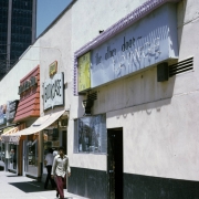 View of the Other Door Lounge, a gay bar at 15 Broadway in the North Capitol Hill neighborhood, Denver, Colorado. The one story commercial style building has a stucco exterior with one window. The bar is next door to the Bookcase bookstore. The building was built around 1920.