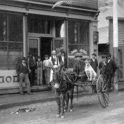 Street scene in front of Georgetown, Colorado saloon. Chan Gow, a Chinese man, sits in a two wheel cart being drawn by a burro.