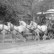 View of a Flower Carnival parade entry, Colorado Springs, El Paso County, Colorado; shows "China Jim," a Chinese businessman, in a suit and planter hat with a wagon and team. Chinese in skullcaps peek over the float decorated with paper lanterns, umbrellas, and fans.