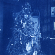 View of a decorated Christmas tree and presents in a house near the mining town of American City (Gilpin County), Colorado. Portraits of three women and others are hung on the walls.
