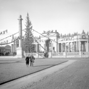 A couple stands on the grassy plaza in front of the Greek Amphitheater, an arched colonnade of Ionic columns, in Civic Center in Denver, Colorado. The structures are decorated with garland, wreaths, and a replica of Santa Claus and eight reindeer.