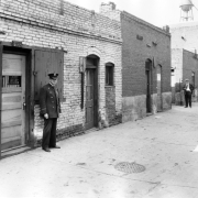 A Chinese man, a white man, and a police officer stand near a building at 2032 Hop Alley (between Wazee and Blake Streets) near 20th (Twentieth) Street in Denver, Colorado.