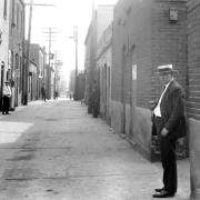 Men and police officers stand in Hop Alley (between Blake and Wazee Streets) in Denver, Colorado. A sign on a brick building reads: "Colored Boxing Show Friday June 27 [...]".