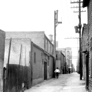 A man walks in Hop Alley (between Wazee and Blake Streets) in Denver, Colorado. A water tower is on the roof of a building in the distance.