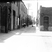 Men and boys stand in Hop Alley (between Market &amp; Blake Streets) in Denver, Colorado. An automobile and a sign that reads: "Poultry" are in the distance.