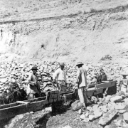 Chinese miners work at a sluice possibly in Colorado. They wear long shirts and wide-brimmed hats.