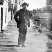 A Chinese man poses on a wooden sidewalk near a business district possibly in Colorado. A nearby sign on a building reads: "[?]ng Lee [La]undry".