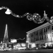 Nighttime view of Christmas decorations on Broadway in Denver, Colorado. Signs on nearby buildings read: "Ellsworth Hotel," and "Pennys Open."