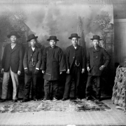 Studio portrait of Chinese-American men who include Wa Chin and Tang Ya-Shun in Georgetown (Clear Creek County), Colorado. Wa Chin wears a long shirt and wide-brimmed hat. Tang Ya-Shun wears a suit and watch chain with a charm.