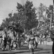 Men (Chinese - American) dressed in traditional chinese clothing walk along side a chinese dragon during the Festival of Mountain and Plain parade in Denver, Colorado. Spectators watch from the grandstands.