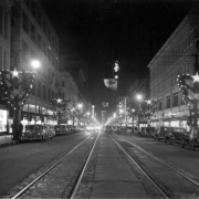 Nighttime view of 16th (Sixteenth) Street in downtown Denver, Colorado. Automobiles are parked near the edge of the street. Lightposts are decorated with Christmas lights and greenery.