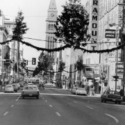 View of 16th (Sixteenth) Street in downtown Denver, Colorado. The Daniels &amp; Fisher Tower is in the distance. Signs read: "Denver Arlo Guthrie 'Alice's Restaurant'," "Duplers Furs," "[Pa]ramount," "Swift Steak House," "Douglas Optical," and "Security Nation[al]." Shows garlands with Christmas trees hung across the street.