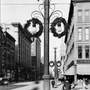 View of 16th (Sixteenth) Street in Denver, Colorado; shows pedestrians, light poles, Christmas wreaths, office buildings, and the Daniels and Fisher tower.