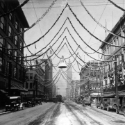 View of 16th (Sixteenth) Street in Denver, Colorado; shows autos and trucks, office buildings, a streetcar, the Daniels and Fisher tower, and Christmas decorations including a bell.