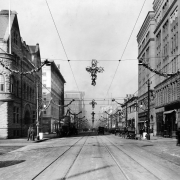 View of the intersection of Glenarm and  17th (Seventeenth) Streets in Denver, Colorado; shows the Denver Club, the Johnson Building, automobiles, Christmas ornaments, and pedestrians.