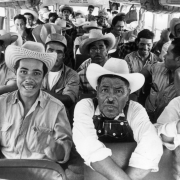 Mexican migrant workers sit in a bus near Fort Lupton (Weld County), Colorado. They wear wide-brimmed hats. One man wears overalls.