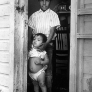 A Mexican American boy and a toddler pose in the doorway of a migrant laborer's house near Fort Lupton (Weld County), Colorado. The small boy wears a shirt and diaper.