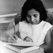 Romana Bora, a Mexican American girl, sits at a school desk in Platteville (Weld County), Colorado. She writes with a pencil and wears a dress.