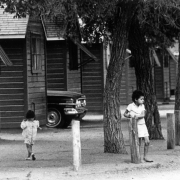A Hispanic boy and girl play near a group of homes in Fort Lupton (Weld County), Colorado. An automobile is parked nearby.