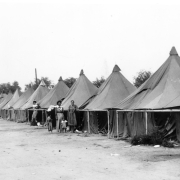 Hispanic women and children stand near a group of tents in Fort Lupton (Weld County), Colorado. The women wear dresses.