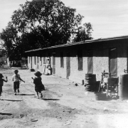 Hispanic children play near a house at a migrant workers' camp near Manzanola (Otero County), Colorado. A manual washing machine, lumber, and large metal drum are nearby.