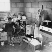 A Hispanic boy and girl pose in the kitchen of a house in Colorado. Cooking supplies, food, pots, and pans are in the room. A stove is nearby.