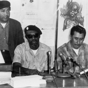 Shirley Sandage and Migrants in Action members Rudolfo Dominguez, Jim Mason, Gregorio Salazar and Leonel Sanchez give a press conference concerning the living conditions of migrant workers in Fort Lupton (Weld County), Colorado. Rudolfo Dominguez, Jim Mason, and Leonel Sanchez wear berets.