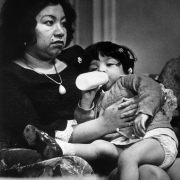 Mrs. Lionel Sanchez, a Mexican American, holds her daughter during a hunger strike to protest living conditions of migrant workers near Fort Lupton (Weld County), Colorado. The girl drinks from a baby bottle.