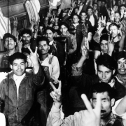 Mexican migrant workers sit in a bus in Colorado. They hold their hands up in a sign for "victory."