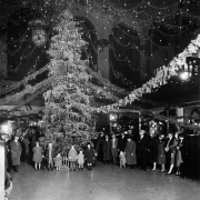 Interior view of the Union Station, in Denver, Colorado. Children, women, and men pose by a Christmas tree, garlands, and decorations.