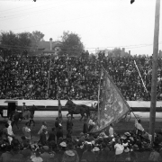 Chinese men carry banners and ride on horseback, part of the Festival of Mountain and Plain, in Denver, Colorado. Spectators line the street and sit in nearby grandstands.