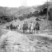 Men who include President Theodore Roosevelt and his guide Henry Bunn, Sr. ride on horseback as they return from a hunting trip near Glenwood Springs (Garfield County), Colorado. Horse-drawn buggies are behind the group.