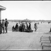 Ice skating on City Park Lake, Denver, Colorado; view east to Museum of Natural History building under construction in 1901; shows edge of City Park bandstand far left and groups seated on park bench on sandy shore.