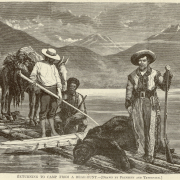 Men and a dead bear are on a raft on a lake in the mountains. The hunter holds a rifle and wears a fur-lined coat, buckskin pants with bead or quill work, fringe, moccasins and a wide-brimmed hat. A man in knickers and a man in a fringed jacket are beside a pack mule.
