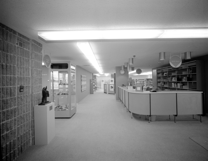 Interior view of the Bear Valley Branch of the Denver Public Library in the Harvey Park South neighborhood of Denver, Colorado; decor includes display cases, a curved check-out counter, a sculpture, and rough bricks.