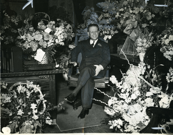 Governor Carr on a chair surrounded by bouquets of flowers