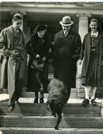 Governor Carr and family well dressed, outside of their home, a black dog leads the way