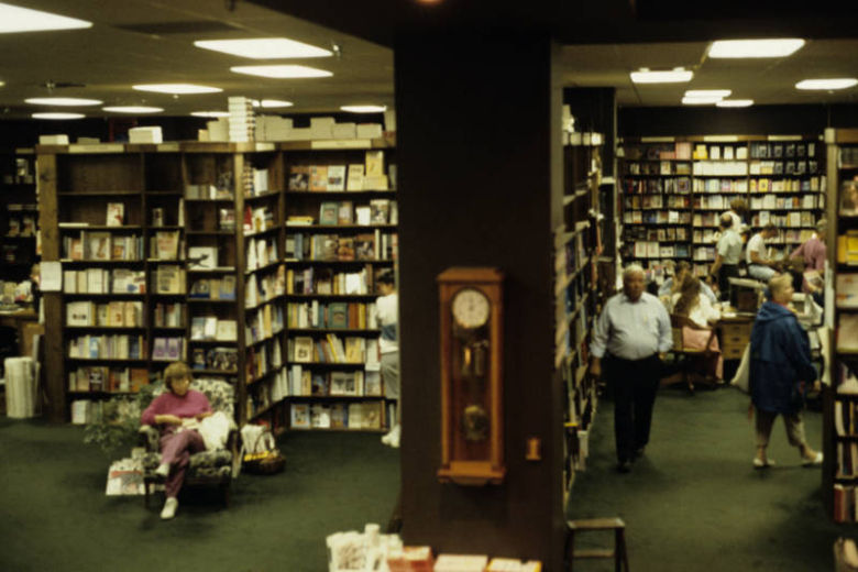 View of the interior of the Tattered Cover Bookstore at 2955 East 1st (First) Avenue in the Cherry Creek Neighborhood of Denver, Colorado. Shows bookshelves, customers and staff. A case clock is on a square column and a woman reads in an overstuffed chair.