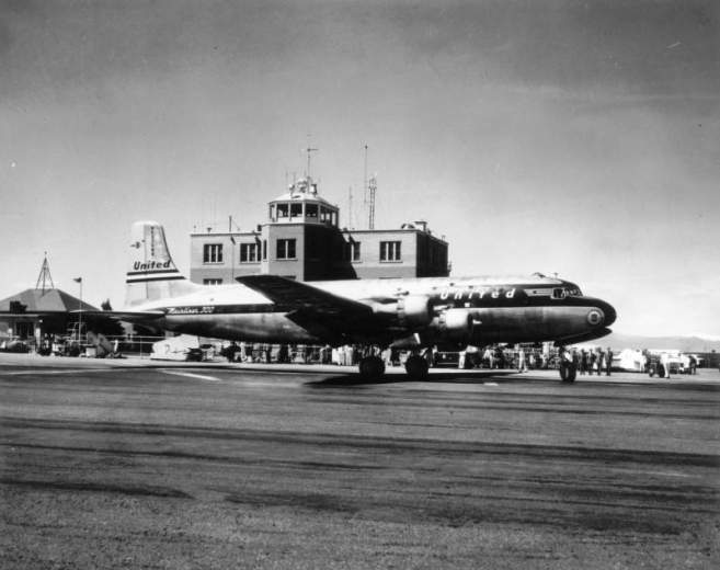 Stapleton Airport, Denver, Colorado, United Airlines passenger jet "Mainliner 300 NC37508" is on the tarmac. People stand behind the airplane; the terminal and control tower are in the background. Antennae and wind instruments top the roof.