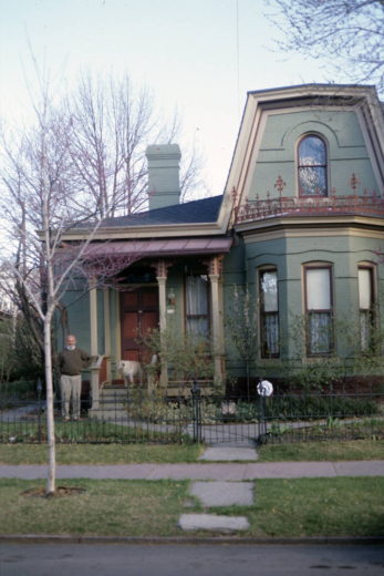 View of the Scobey House (c. 1882) at 2826 Curtis Street in the Five Points neighborhood of Denver, Colorado. This one-and-one-half-story brick residence shows characteristics of Second Empire and Late Victorian styles. Features include wood trim, iron cresting, and a mansard-roof extension. William Allen West, the owner, is standing next to the porch decorated with scroll-sawn brackets.