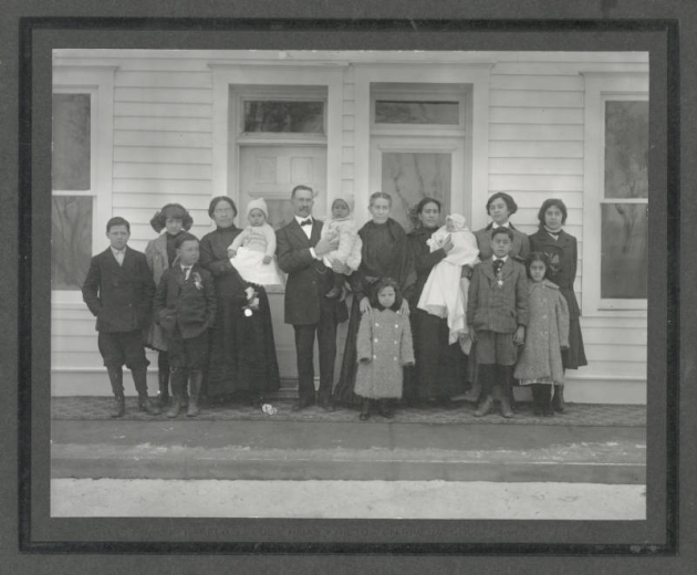 Group portrait of Colorado State Senator Casimiro Barela, his wife Damiana Rivera de Barela, their daughters and grandchildren on the porch of their house (Rancho de Rivera) in Rivera (Las Animas County), Colorado. Senator Barela holds an unidentified grandchild and his wife stand beside him with her hands on the shoulders of a young girl.
