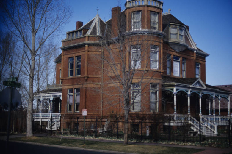 View of the facade and west elevation of the Lumber Baron Inn & Gardens, a bed and breakfast at 2555 West 37th Avenue in the Highland neighborhood of Denver, Colorado.  The mansion was built in 1890 for John Mouat, a Scottish immigrant who had amassed a fortune in lumber. The building has large front and back porches with decorative spindling.  The house also has a three story turret and prominent oriel window on the third story.  The building is part of the Potter Highlands Historic District.