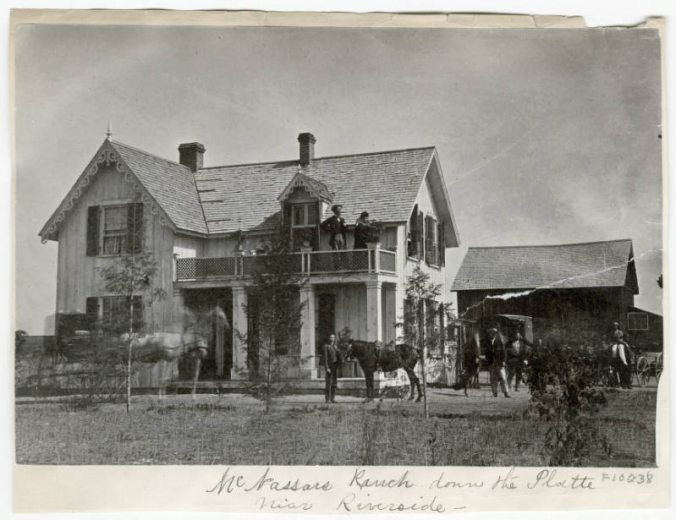 Photograph of the McNassar's ranch home located in the Argo neighborhood of Denver, Colorado.  Several people and animals stand around the main house in various wagons and buggies.