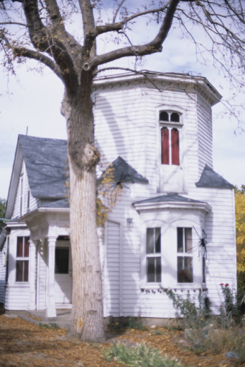 View of 2633 West 37th (Thirty-Seventh) Avenue in the Highland neighborhood, Denver, Colorado. The two-story wood modified Second-Empire style structure has a white exterior. The house has two prominent bay window on the first story and a small covered entrance on the west end of the facade. The second story has an hexagonal turret. The structure is in the Potter Highlands historic district.