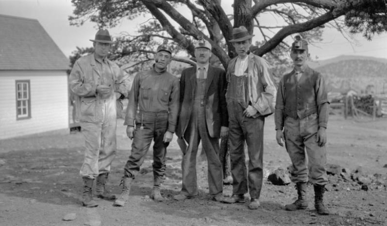 Five male employees of the Rocky Mountain Fuel Company, three of whom wear head lamps, pose in front of a tree, Colorado.
