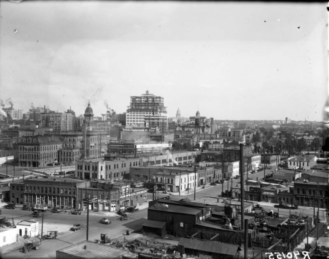 An aerial view of Downtown Denver from the west side of Cherry Creek. Shows the Telephone Company under construction, the old Denver City Hall, Denver Auditorium and the State Capitol.
